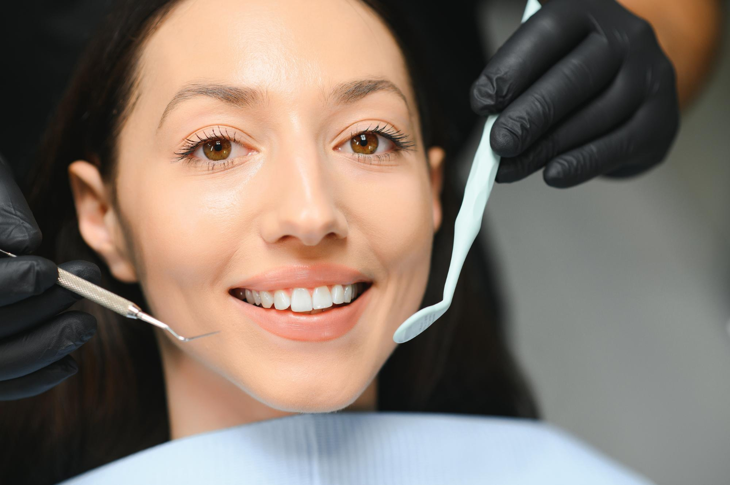 63268 Smiling woman at the dentist, with dental tools held near her mouth by gloved hands.